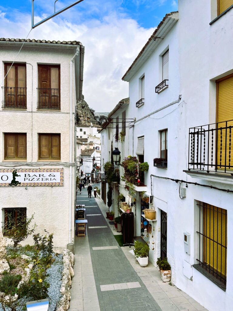 Узкая улочка старого города Гуадалест с белыми домами и цветами на балконах, провинция Аликанте, Испания